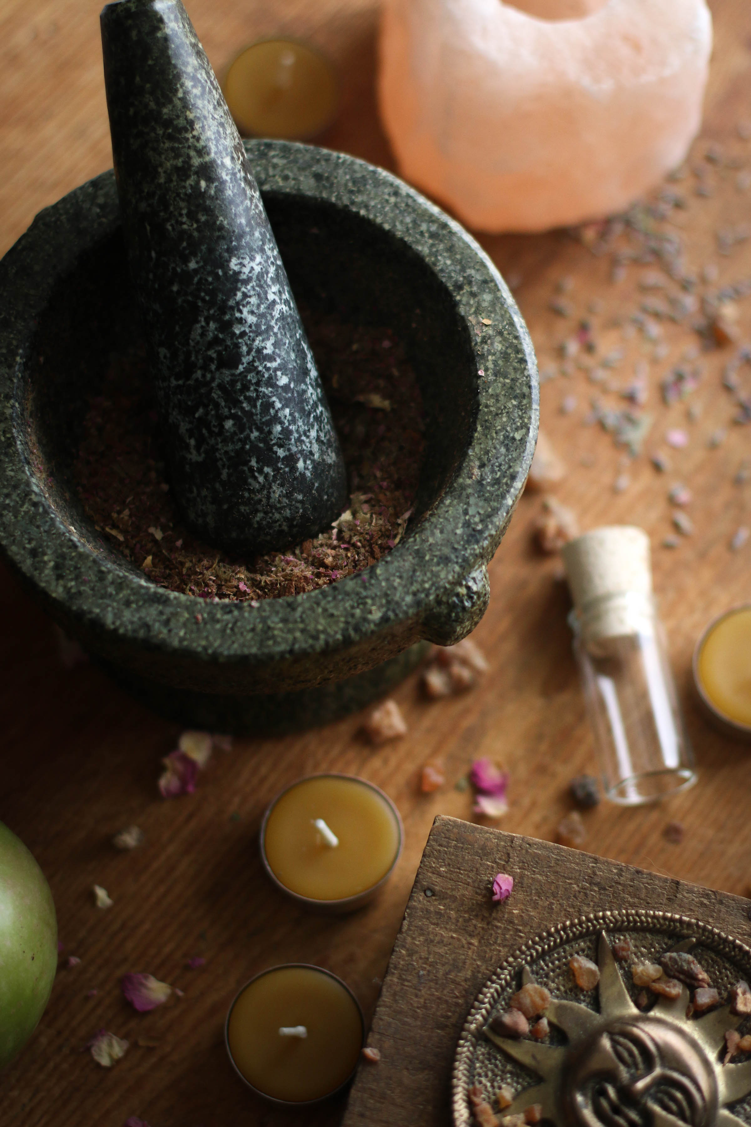 Mortar and pestle on top of a wooden table with a glass vial and beeswax candles nearby