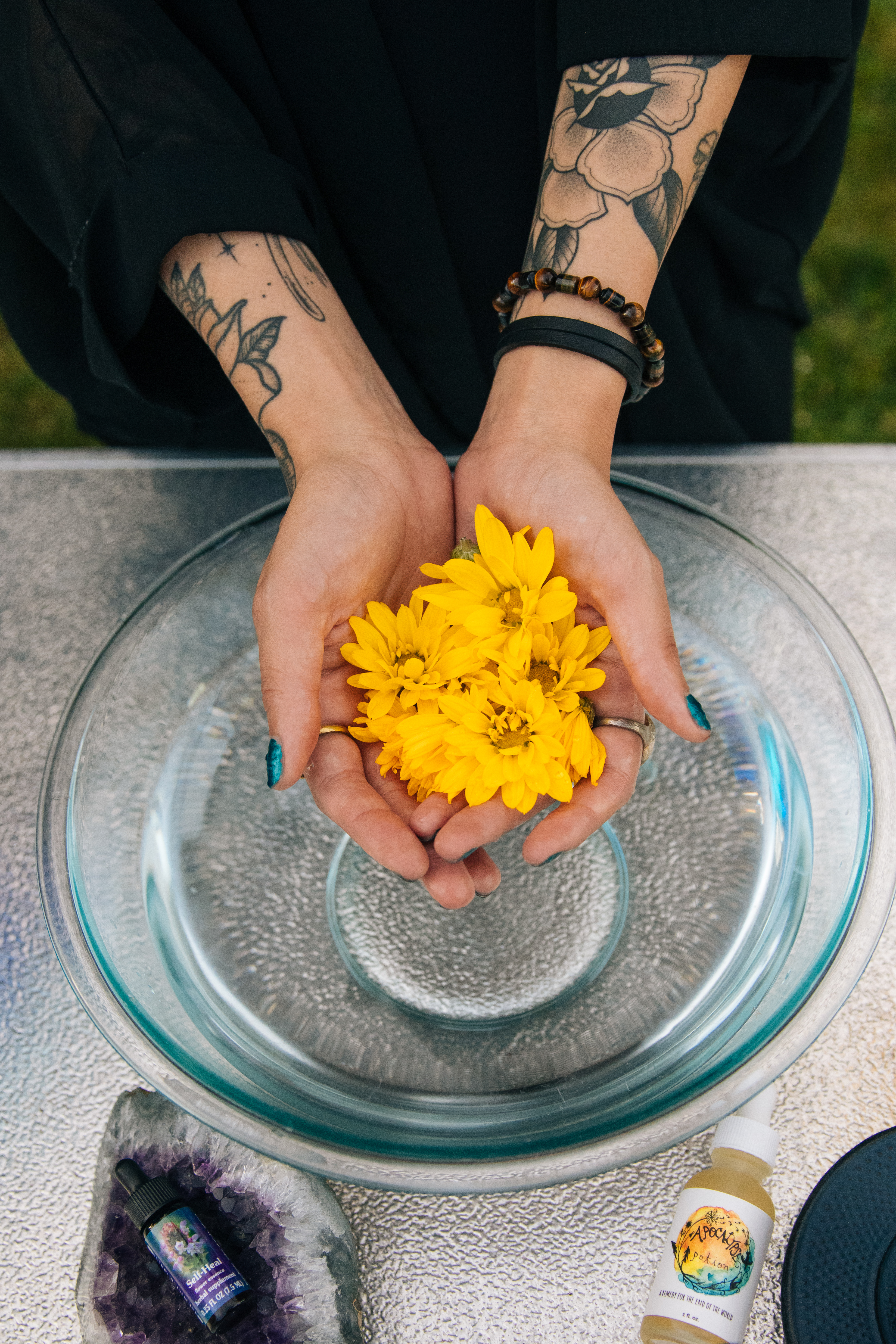 young-woman-with-tattooed-arms-holding-yellow-flowers-over-glass-bowl-of-water-for-summer-solstice-ritual