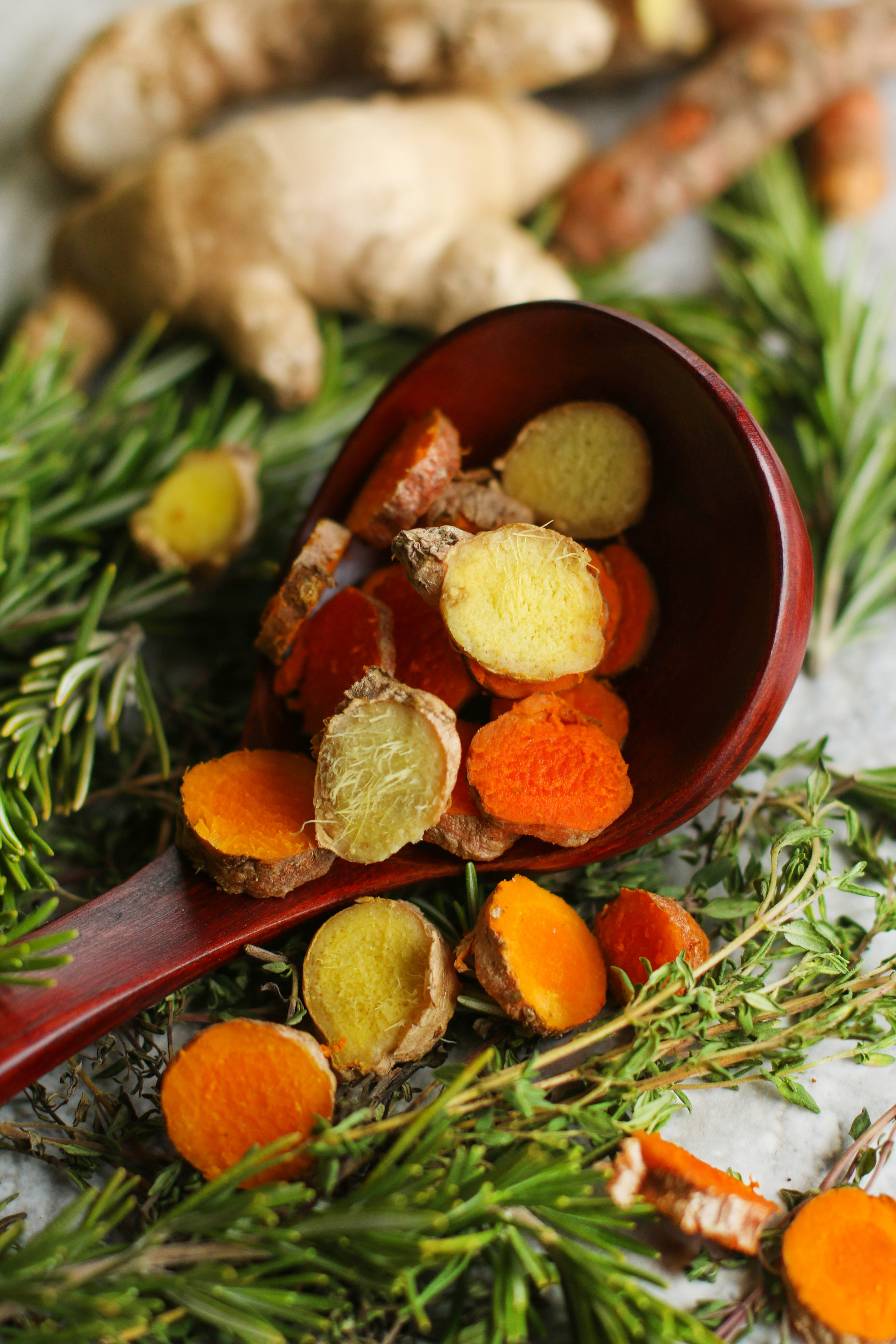 sliced-fresh-turmeric-and-ginger-root-on-wooden-spoon-with-fresh-rosemary-thyme-and-other-herbs