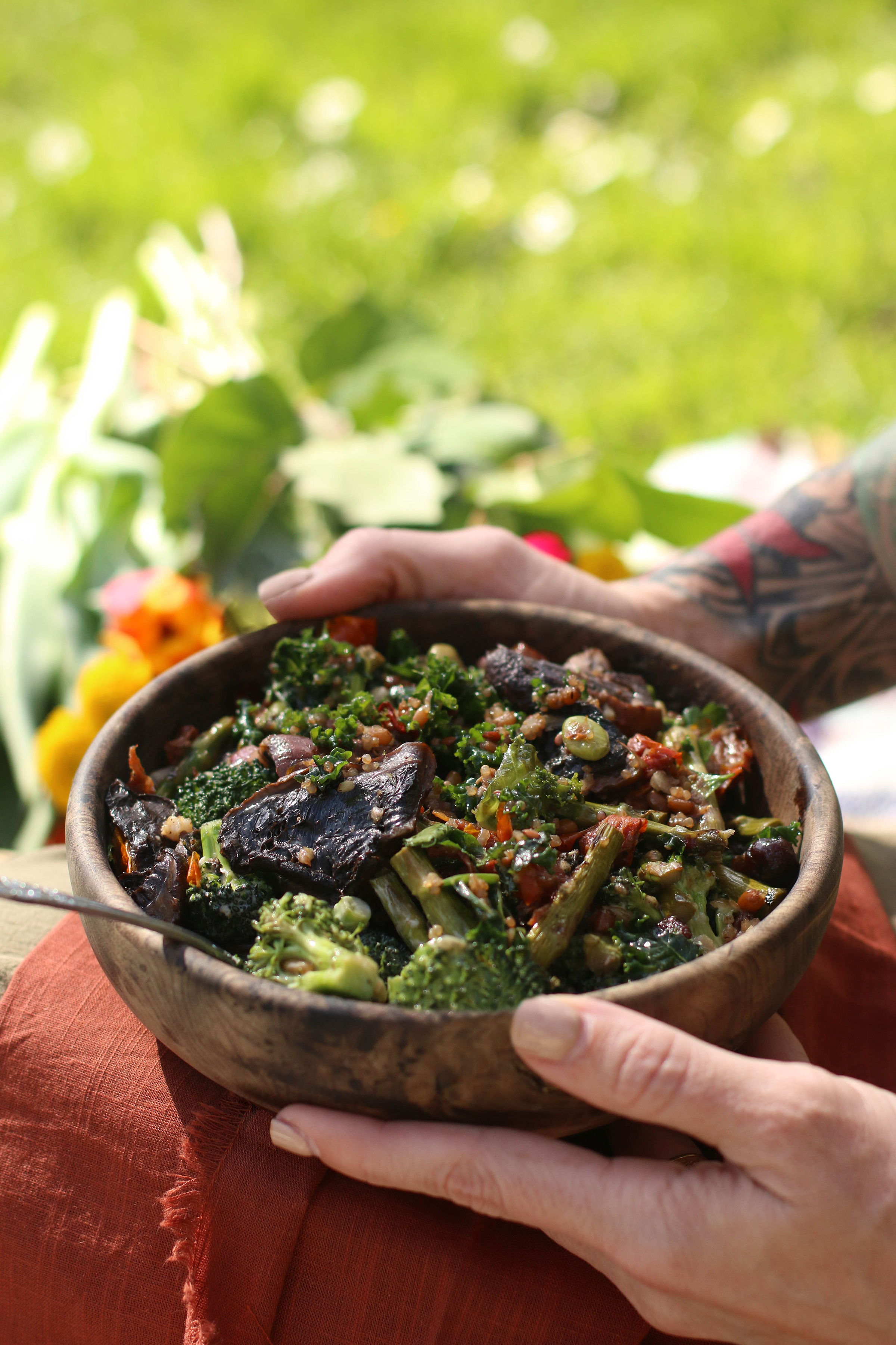 hands-holding-wooden-bowl-of-fresh-spring-greens-and-mushrooms-sitting-outdoors