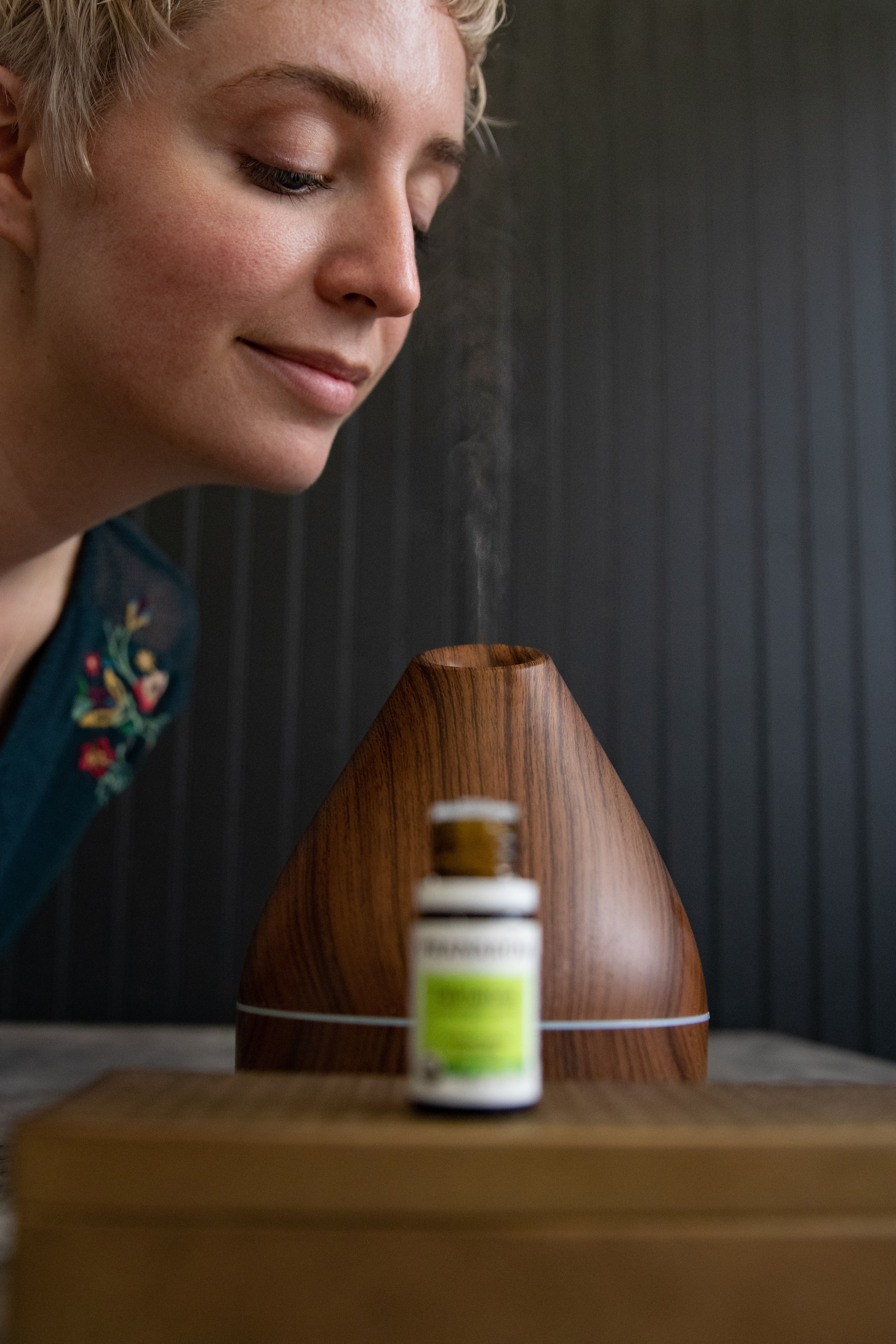 young-blonde-woman-with-short-hair-inhaling-steam-from-a-wooden-essential-oil-diffuser