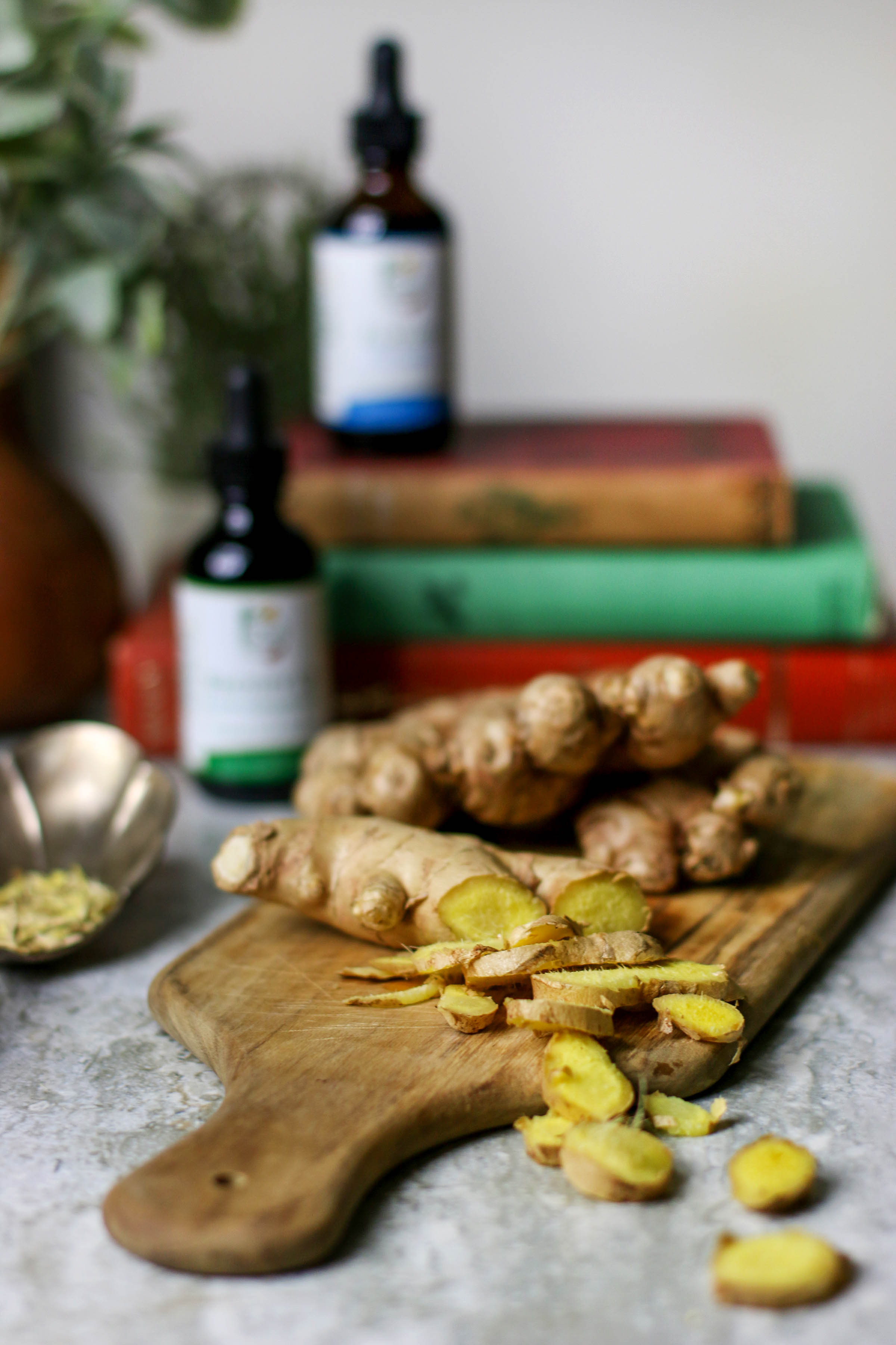 Fresh ginger root chopped into discs on wooden cutting board with books and tincture in background.