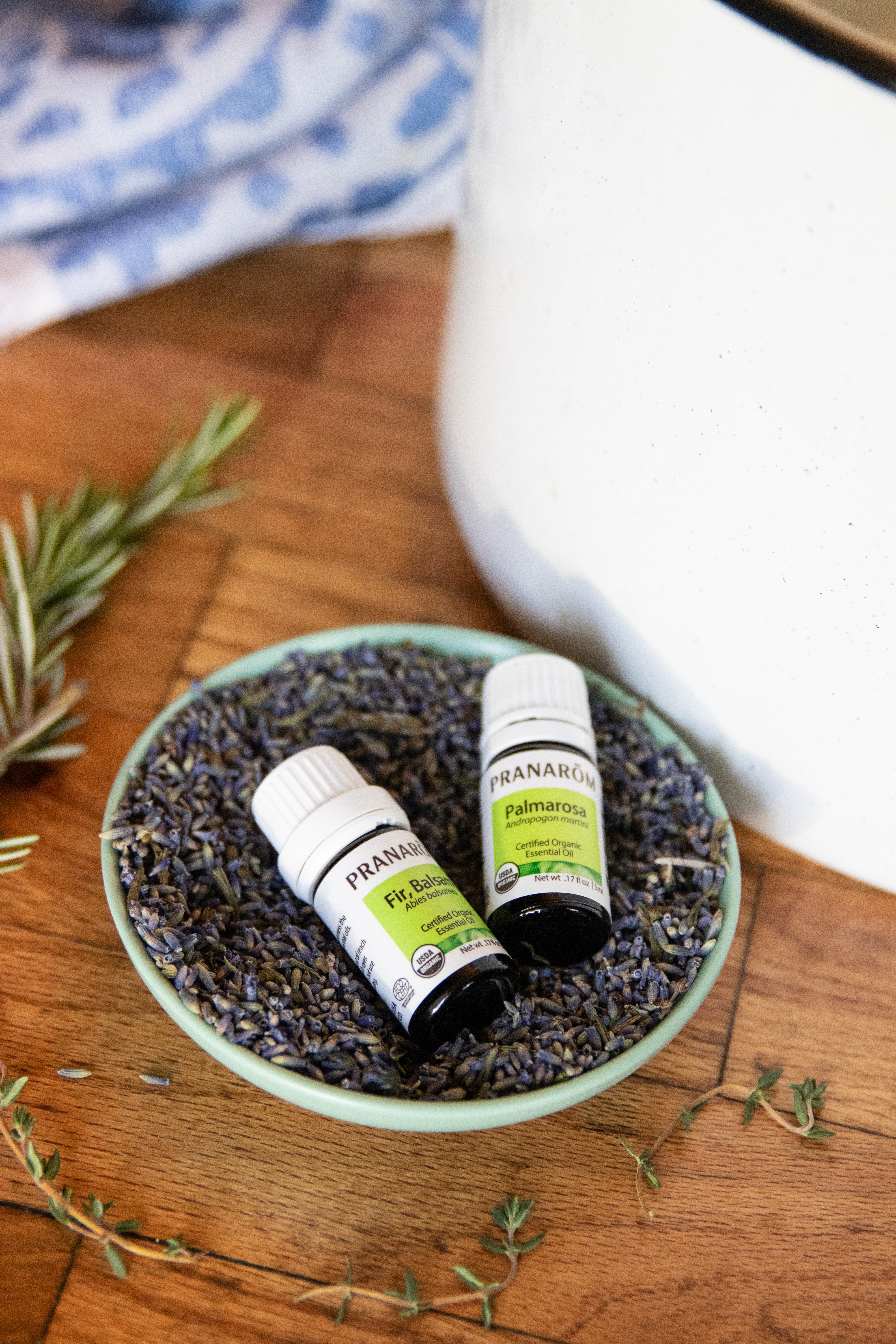 two-bottles-of-essential-oils-sitting-dish-of-dried-lavender-with-diffuser-in-background