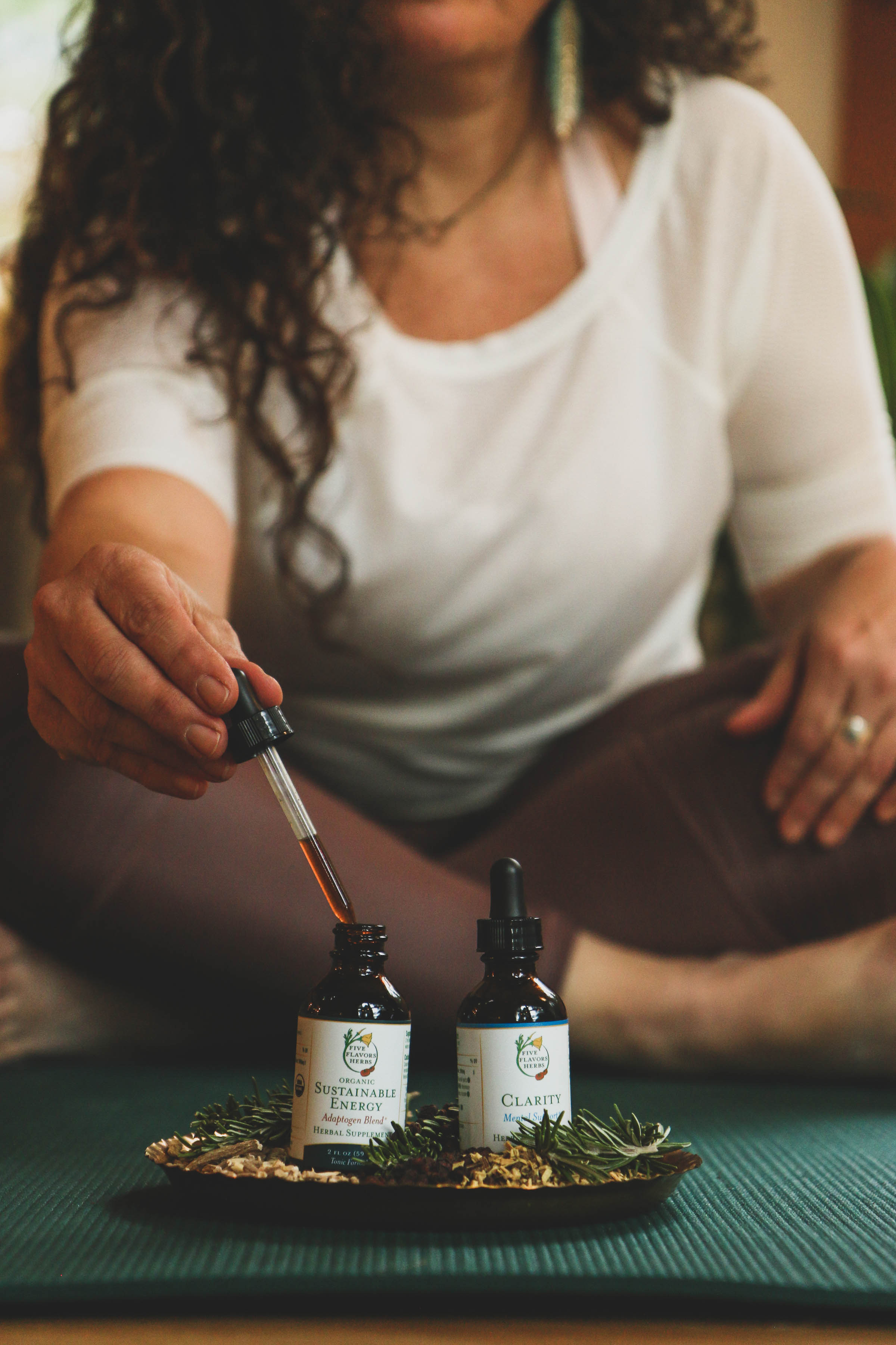 bottles-of-herbal-extracts-from-five-flavors-herbs-with-woman-in-yoga-gear-holding-dropper-of-tincture