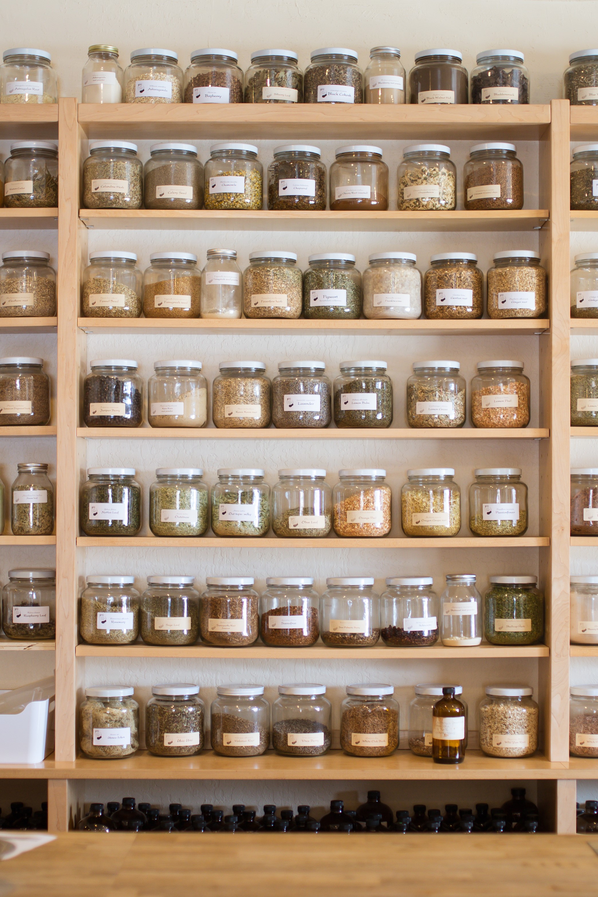 large-glass-jars-of-dried-medicinal-herbs-and-spices-lined-up-on-pale-wood-apothecary-shelves