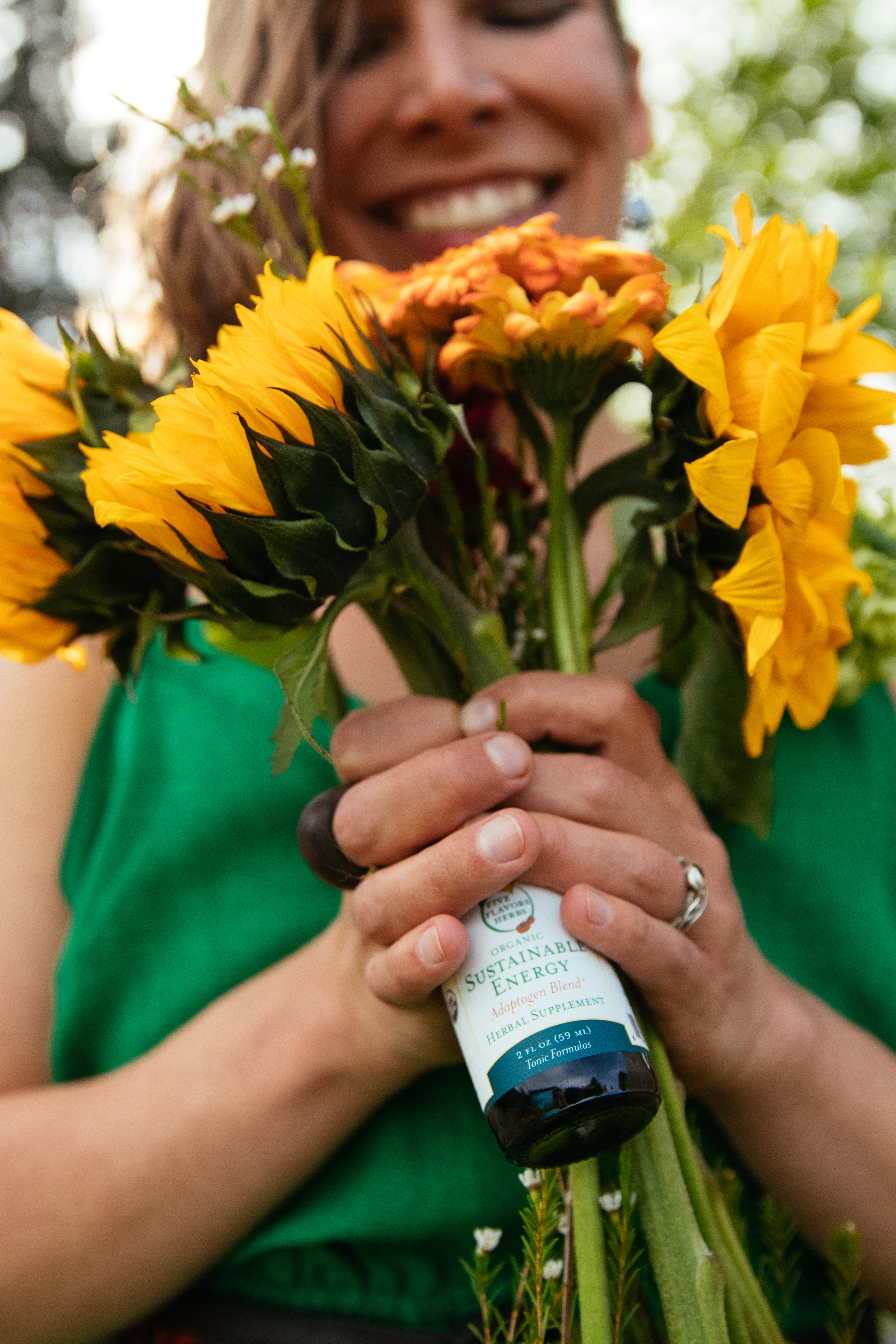 young-woman-in-green-top-holding-bouquet-of-sunflowers-and-glass-dropper-bottle-of-sustainable-energy-tincture-from-five-flavors-herbs