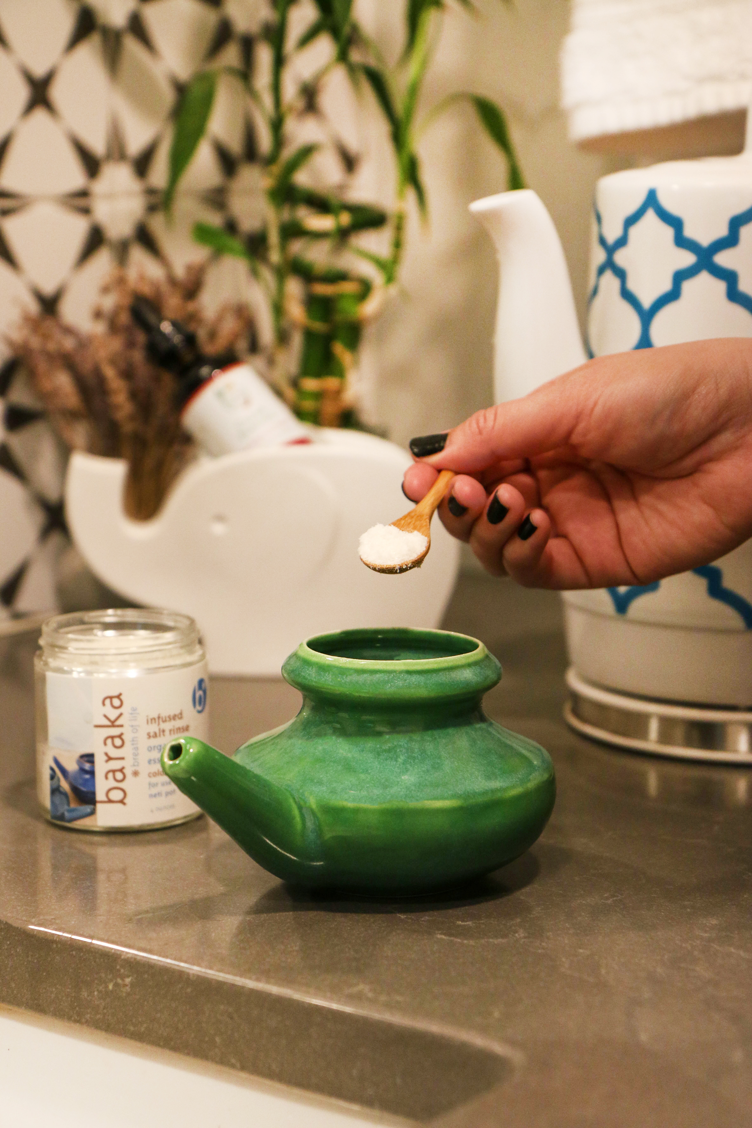 hand-holding-small-wooden-spoon-of-neti-pot-salt-solution-blend-over-green-ceramic-neti-pot