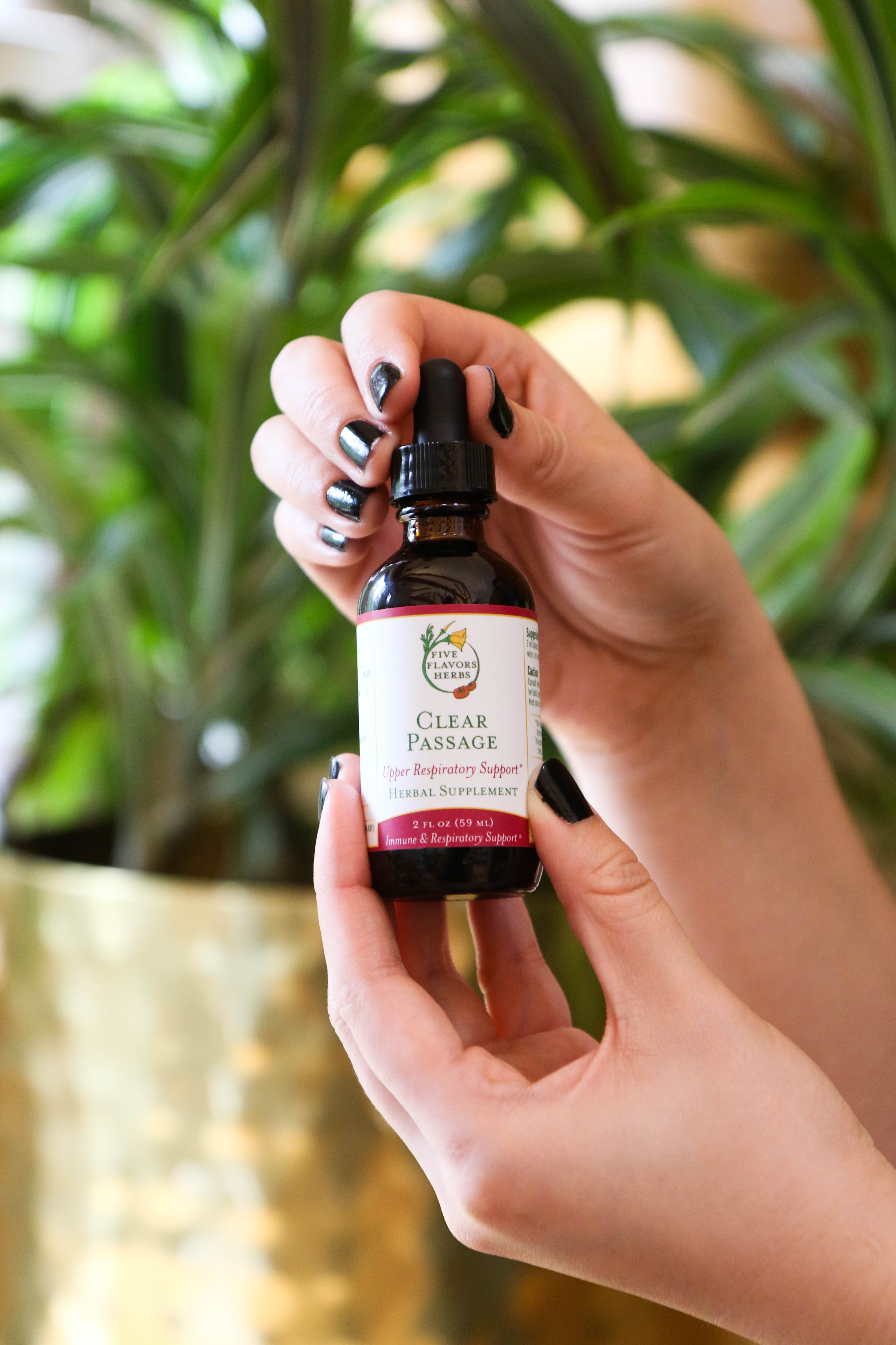 hands-holding-up-amber-glass-bottle-of-clear-passage-upper-respiratory-tincture-with-plants-in-background