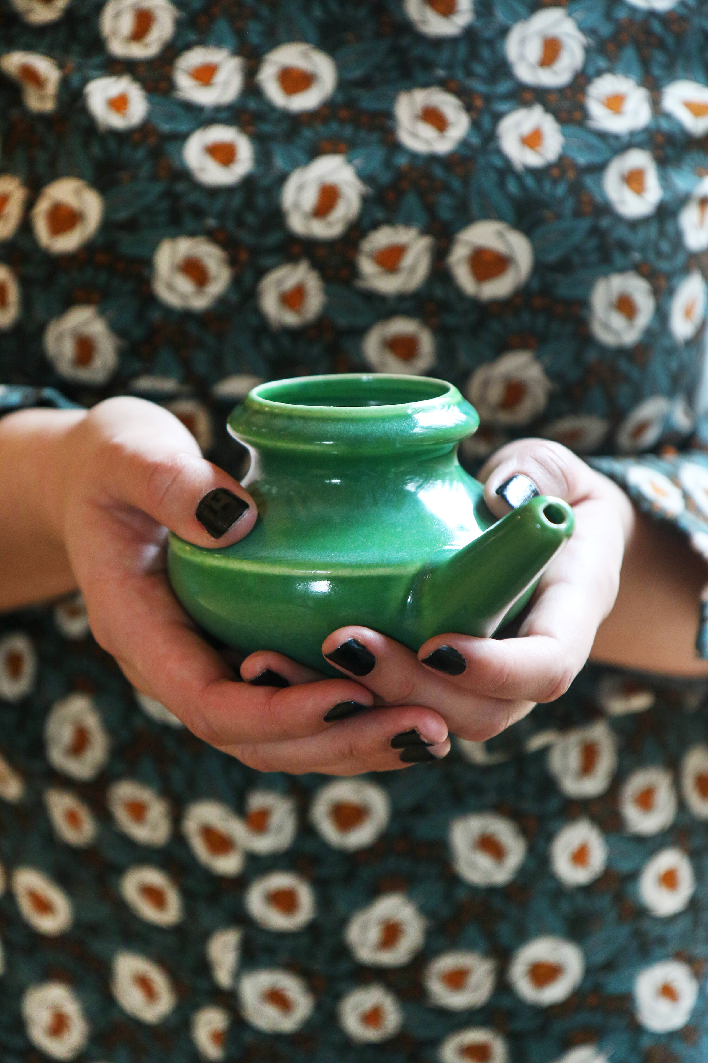 green-ceramic-neti-pot-being-held-in-hands-with-dark-nail-polish-in-front-of-patterned-dress