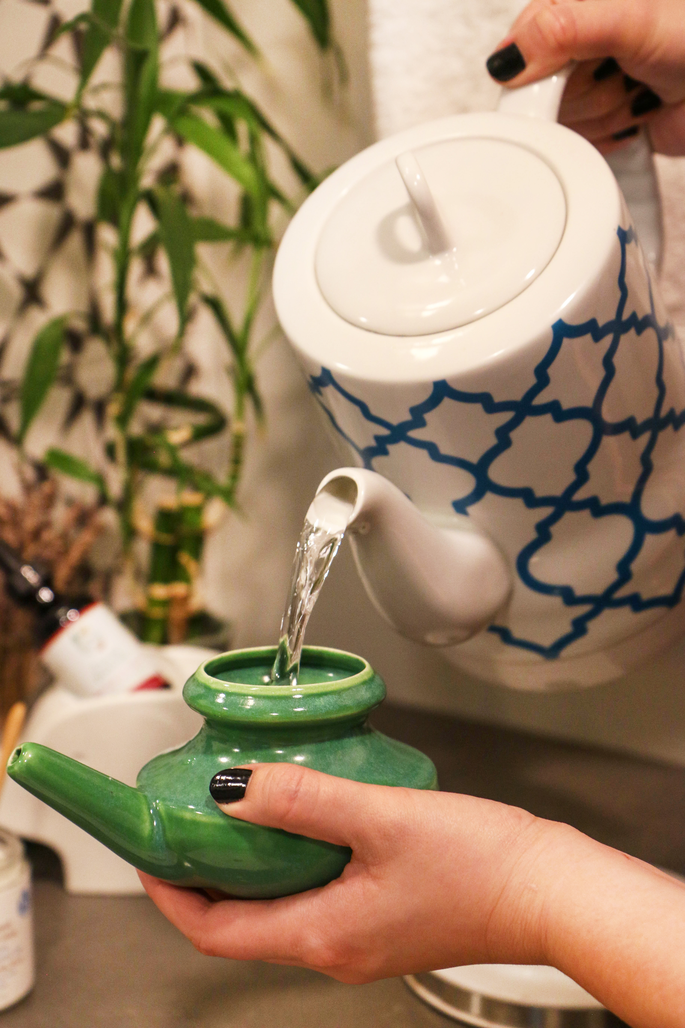 boiled-cooled-water-being-poured-from-white-and-blue-ceramic-kettle-into-green-ceramic-neti-pot