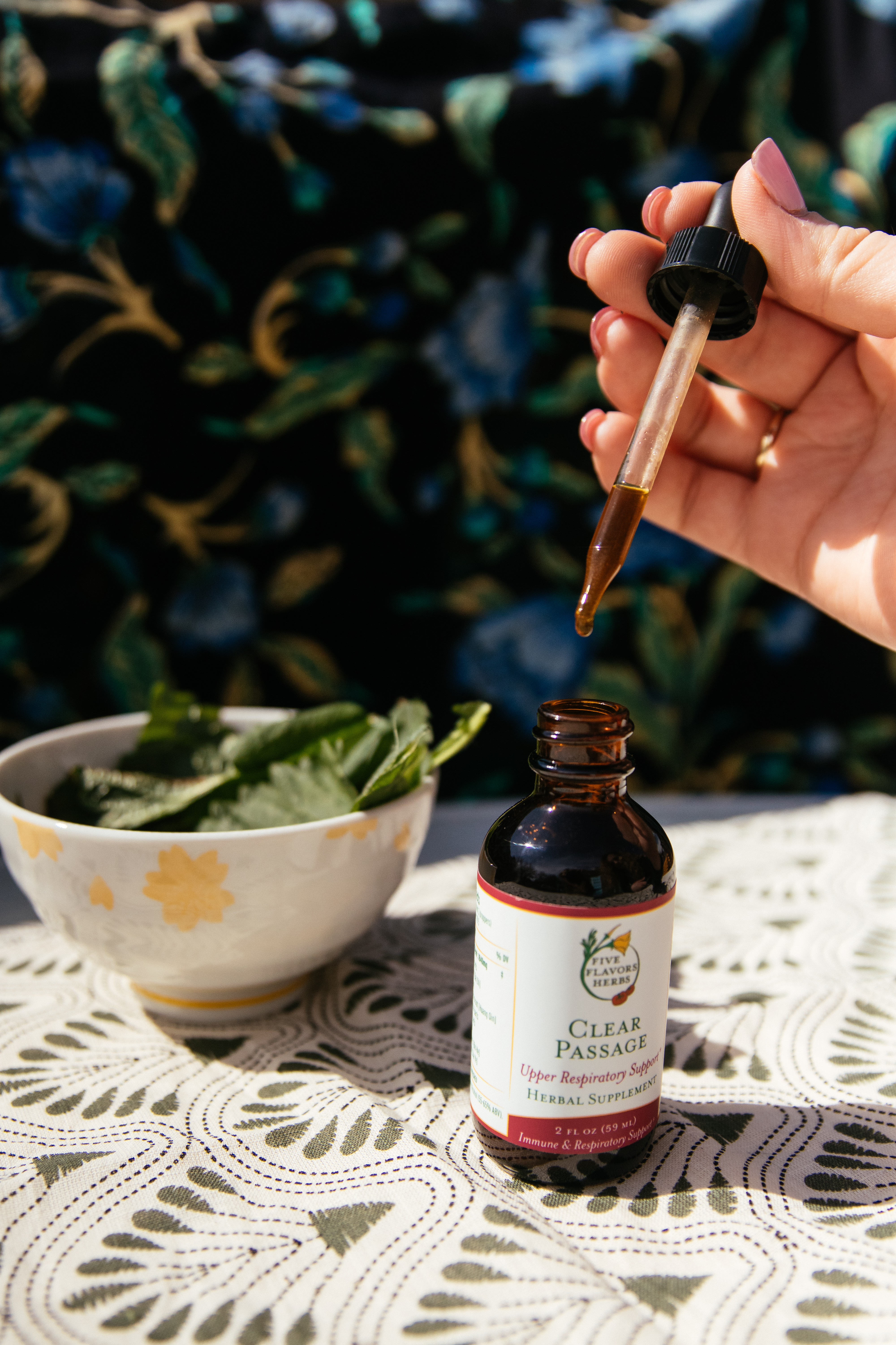 amber-glass-bottle-of-clear-passage-sinus-tincture-on-table-outdoors-with-bowl-of-fresh-nettles-in-background