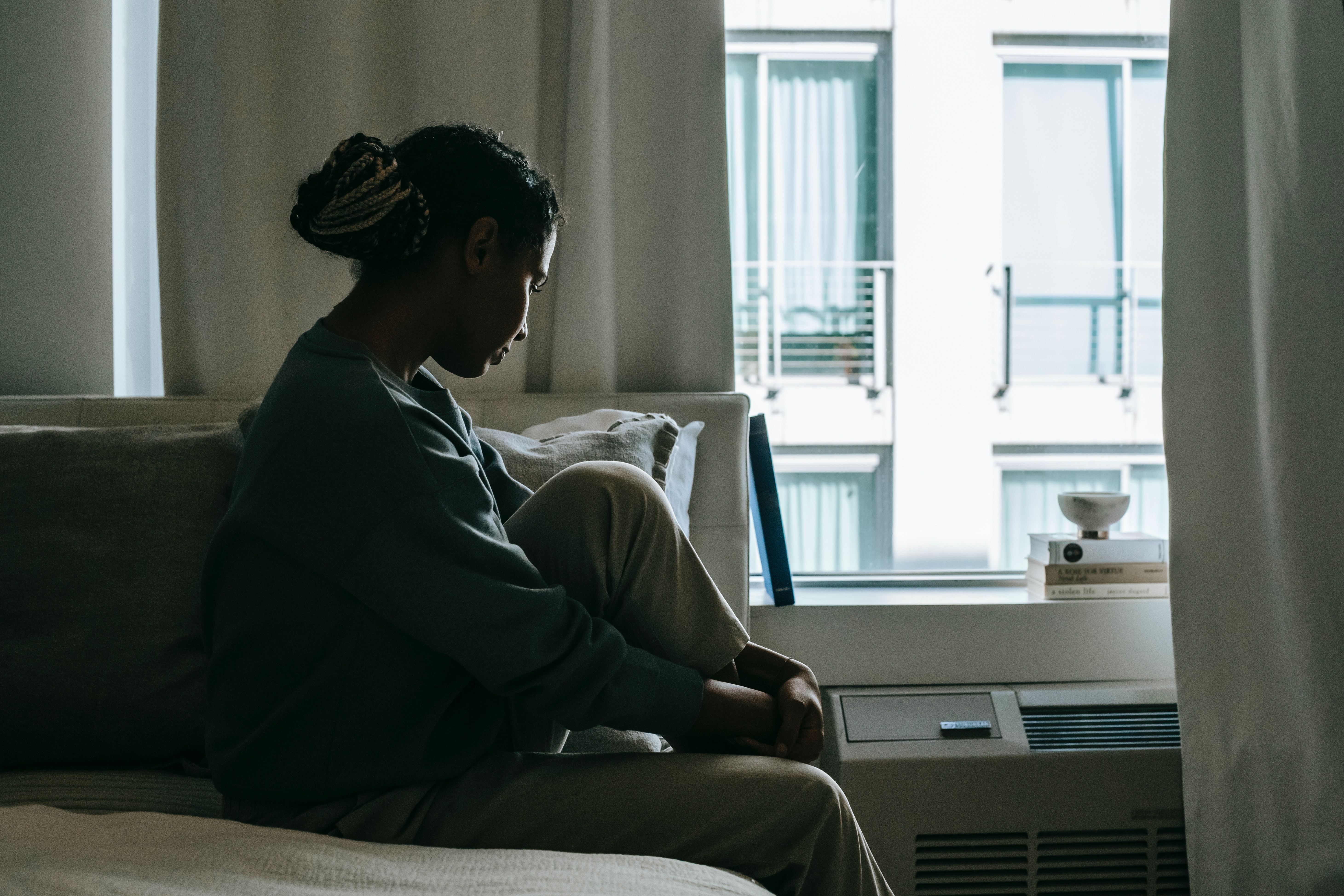 sad-black-woman-sitting-on-bed-by-apartment-window