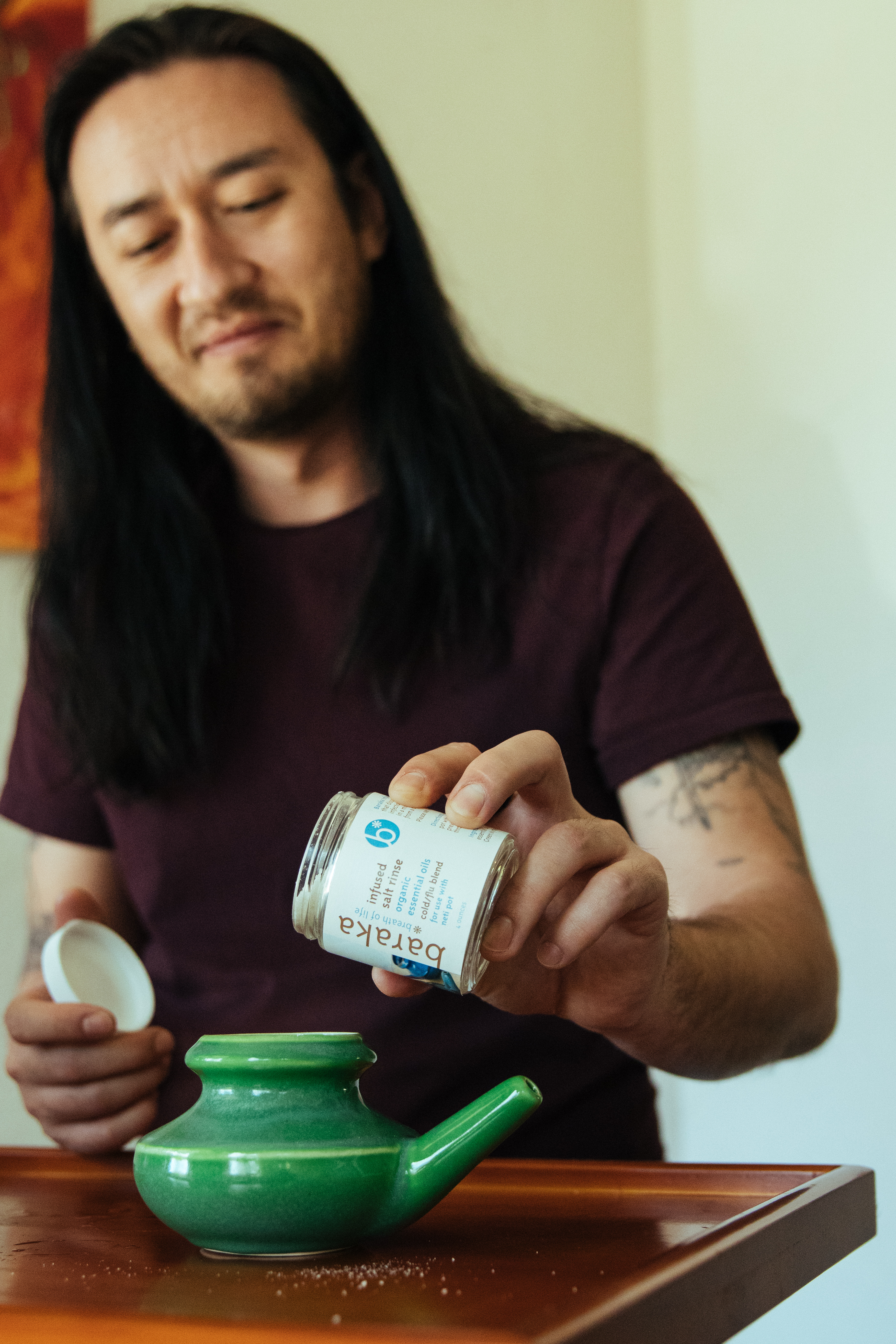 young-man-with-long-hair-and-tattoos-pouring-salt-solution-into-green-ceramic-neti-pot-for-sinus-relief